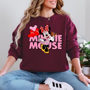 A woman wearing a burgundy sweatshirt with a Minnie Mouse graphic and the text "MINNIE MOOSE" is sitting on the floor.