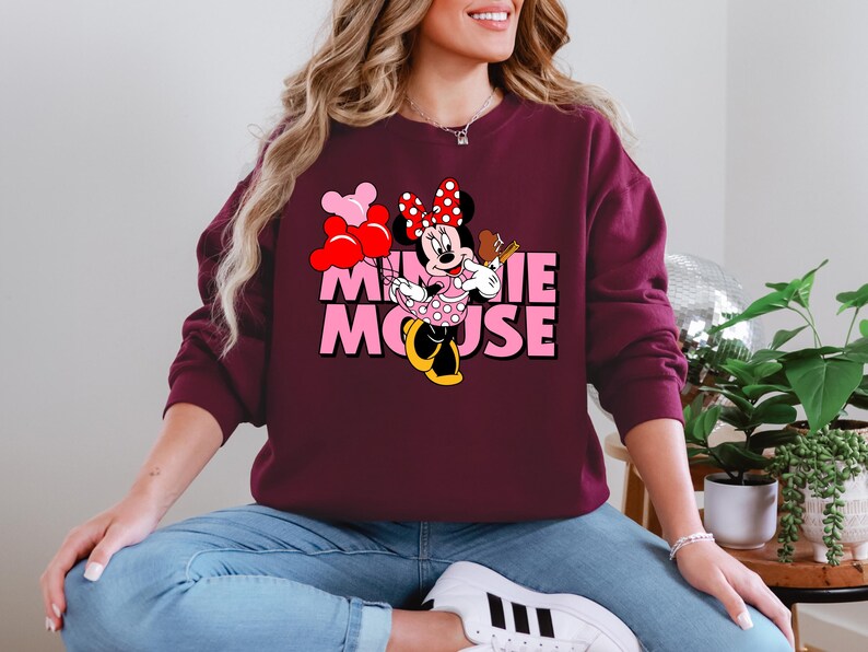A woman wearing a burgundy sweatshirt with a Minnie Mouse graphic and the text "MINNIE MOOSE" is sitting on the floor.