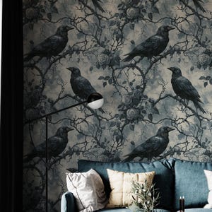 May include: A teal sofa with decorative pillows sits in front of a wall with a crow and floral wallpaper. A black floor lamp and two small white tables with candles and books complete the room's decor.