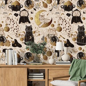 May include: A cream-coloured wallpaper design with a repeating pattern of cats in witch costumes, moons, stars, and cauldrons in gold and black. A wooden cabinet with books, a lamp, and vases is in the foreground, adding depth to the scene.