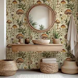 Op de afbeelding: Een badkamer met een ronde spiegel van gevlochten materiaal, een houten wastafel met een stenen wastafel en behang met paddenstoelpatroon. Gevlochten manden en een plant in een pot dragen bij aan de natuurlijke uitstraling. Een beige handdoek hangt aan de muur.
