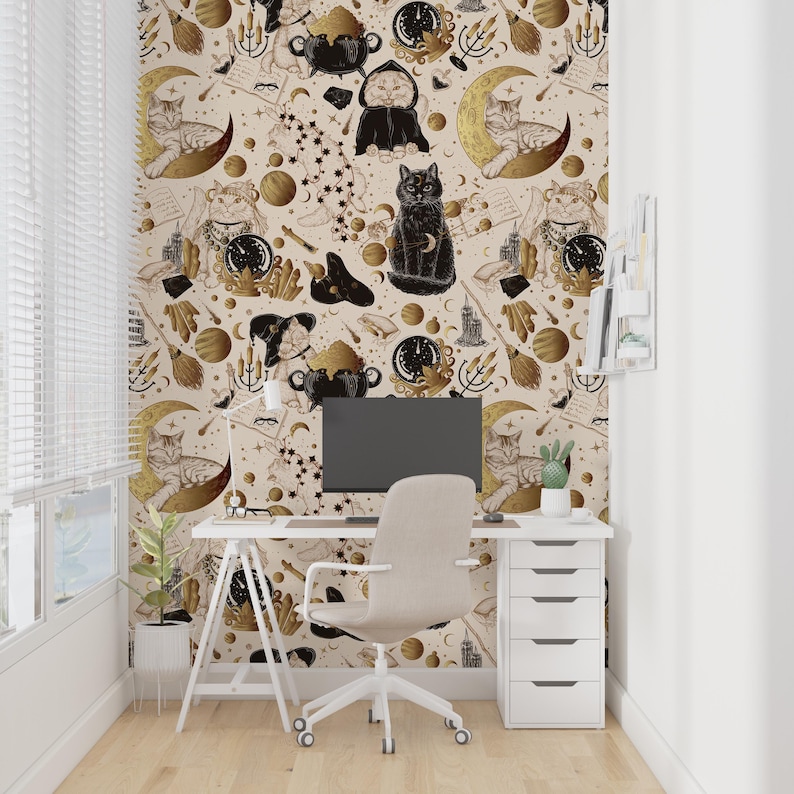 May include: A home office featuring a white desk, chair, and computer. The wallpaper has a repeating pattern of cats, moons, stars, cauldrons, and mystical elements in gold and black on a cream background. A small plant and cactus are on the desk.
