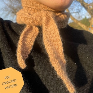 Könnte beinhalten: Nahaufnahme einer gehäkelten Schals in hellbrauner Farbe. Der Schal wird um den Hals einer Person getragen, die ein schwarzes Hemd trägt. Der Text "PDF CROCHET PATTERN" ist in der linken unteren Ecke des Bildes sichtbar.
