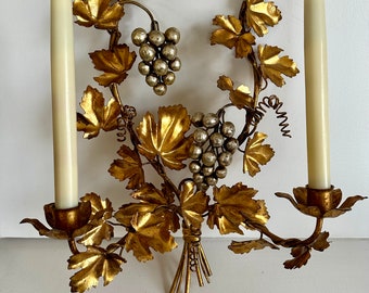 May include: Gold metal wall sconce with two candle holders and a grapevine design. The sconce features silver grapes and leaves.