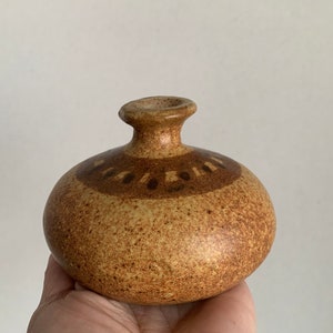 May include: A small, round, brown ceramic vase with a speckled glaze and a brown band of geometric designs around the middle.