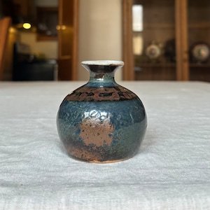 May include: A small, round, blue and brown ceramic vase with a white rim.