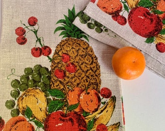 May include: A set of two linen tea towels with a fruit motif. The towels feature a pineapple, cherries, grapes, peaches, apples, and bananas. The towels are white with a green, yellow, orange, and red design. The towels have the text "FRUITS" and "Parisian Prints All Pure Linen" printed on them.