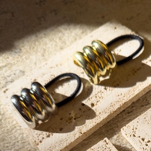 Puede incluir: Cuatro coleteros en pequeñas baldosas beige. Dos coleteros son dorados y dos son plateados. Los coleteros están hechos de metal y tienen un acabado texturizado.