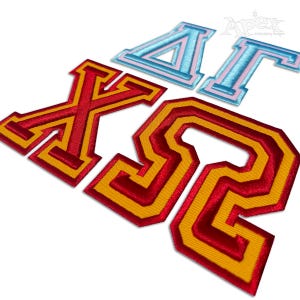 May include: Embroidered patches in various letter and Greek symbol designs. The patches feature a red and yellow color scheme, with some letters in light blue and pink. The patches are likely for apparel or accessories.