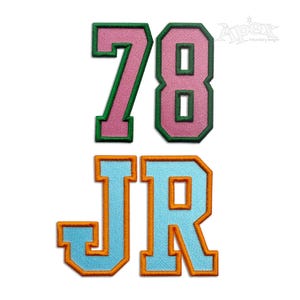 Può includere: Toppe ricamate con i numeri "78" in rosa con bordi verdi e le lettere "JR" in azzurro con bordi arancioni. Le toppe sono progettate in stile collegiale, perfette per personalizzare l'abbigliamento.