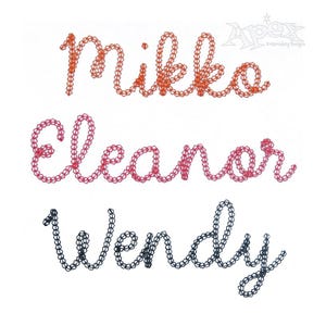May include: Three names, "Mikko", "Eleanor", and "Wendy", are embroidered in a cursive font. "Mikko" and "Eleanor" are embroidered in orange and red thread, while "Wendy" is embroidered in black thread.