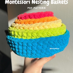 Puede incluir: Un conjunto de cinco cestas de anidación de crochet de colores vivos en tonos de azul, verde, amarillo, naranja y rosa. Las cestas están hechas con un hilo texturizado y están dispuestas en una pila, con la cesta más grande en la parte inferior y la cesta más pequeña en la parte superior. El texto "Montessori Nesting Baskets PDF Pattern" es visible en la parte superior de la imagen. El texto "@KnitsAKnot" es visible en la parte inferior de la imagen.