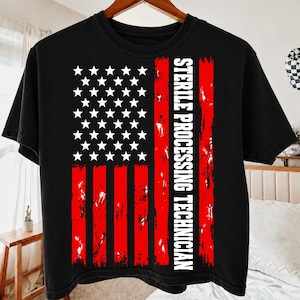 Può includere: Una t-shirt nera a maniche corte con una grafica della bandiera americana invecchiata in rosso e bianco. Il design include una striscia verticale di testo bianco che recita STERILE PROCESSING TECHNICIAN in un font sans-serif.