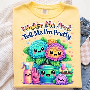 Puede incluir: Camiseta amarilla Comfort Colors con un gráfico colorido. El gráfico presenta flores de dibujos animados en una maceta con el texto "Water Me And Tell Me I'm Pretty". También se muestran herramientas de jardinería y una regadera de dibujos animados.