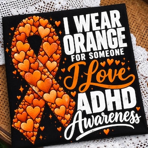 Könnte beinhalten: Ein schwarzes Stoffquadrat mit einer orangefarbenen Schleife, die aus vielen kleinen Herzen besteht. Der Text lautet: I WEAR ORANGE FOR SOMEONE I Love ADHD AWARENESS. Das Design enthält verstreute orangefarbene Herzen und Sternakzente auf dunklem Grund.