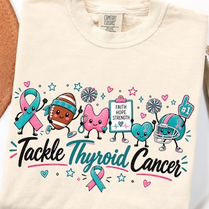 May include: A cream-colored t-shirt featuring a graphic with the text Tackle Thyroid Cancer. The design includes cartoon characters of a ribbon, a football, a thyroid gland, a clipboard with Faith Hope Strength, a heart, and a football helmet.
