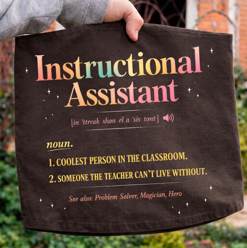 Puede incluir: Una bolsa de mano marr&oacute;n oscuro con las palabras "Instructional Assistant" en texto colorido. La bolsa incluye una definici&oacute;n, que enumera a la persona m&aacute;s genial del aula y a alguien sin quien el profesor no puede vivir.
