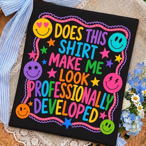 May include: A black t-shirt featuring the colorful text "DOES THIS SHIRT MAKE ME LOOK PROFESSIONALLY DEVELOPED" surrounded by a wavy border, various multi-colored stars, and several smiley faces with different expressions in yellow, pink, and purple.