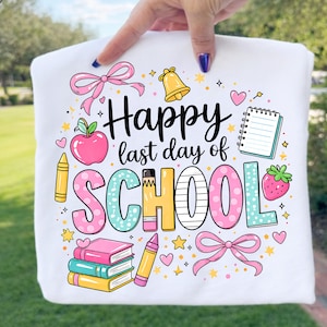 May include: A white t-shirt featuring a colourful graphic with the text Happy last day of SCHOOL. The design includes illustrations of a pink apple, a yellow bell, a spiral notebook, a strawberry, stacked books, crayons, and pink bows.