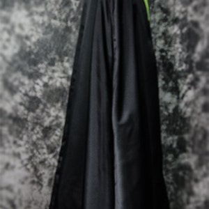May include: A long, black cloak made of a shiny fabric, draped over a mannequin. The cloak has a high collar and a green accent near the neck. The background is a mottled gray and white. The copyright text "&copy; 2013 Lil' Luxe" is visible.