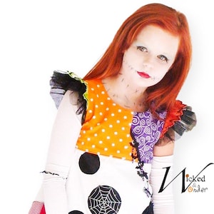 May include: A colorful Halloween costume featuring a patchwork design with orange polka dots, purple swirls, and a spiderweb. The costume has ruffled sleeves and the text "Wicked & Wonder". The person is wearing makeup to match the costume.