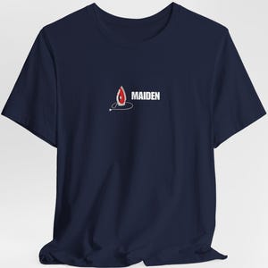 Pode incluir: T-shirt azul marinho com um design gráfico estilizado em vermelho e branco e a palavra "MAIDEN" em branco. O design é uma forma de chama com uma linha branca que se estende dela. A t-shirt tem mangas curtas e gola redonda.