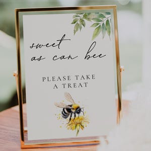 May include: A white sign with gold trim and a bee illustration. The sign reads "sweet as can bee" and "please take a treat".