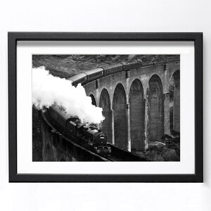 Può includere: Stampa incorniciata in bianco e nero di un treno a vapore che attraversa un ponte ad arco in pietra. Il treno emette una grande nuvola di vapore bianco. Il ponte ha più archi ed è ambientato su uno sfondo di colline e cielo.