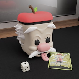 May include: A whimsical, beige-colored container shaped like a cartoon character with an apple lid, a pink nose, and a white mustache. A gold trading card and a white die with black dots are next to the container.