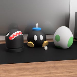 May include: Three cartoon character figurines: a black Bullet Bill with red teeth, a black Bob-omb with a blue fuse, and a white egg with green spots. A small white die is in front of the Bob-omb. The figurines are on a black surface.
