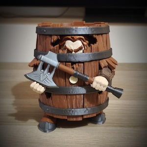 May include: A brown wooden barrel-shaped figurine featuring a character with visible hair and eyebrows peeking through a gap in the top. The figure holds a large silver-colored double-bladed axe with a brown handle and wears metallic-looking boots.