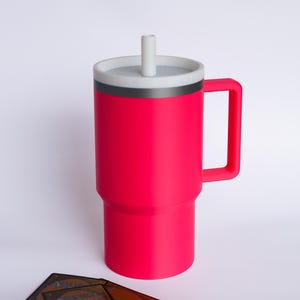 May include: A bright neon pink insulated tumbler with a sturdy side handle, a grey lid, and a matching straw. The tumbler features a stepped cylindrical base and is positioned next to three rectangular trading cards with dark backs.