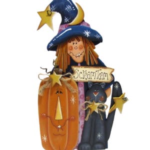 May include: A decorative wooden cutout featuring a witch wearing a blue hat with a yellow star and moon, standing next to an orange pumpkin and a black cat. A sign with the text "Scream Team" is positioned between the witch and the cat.
