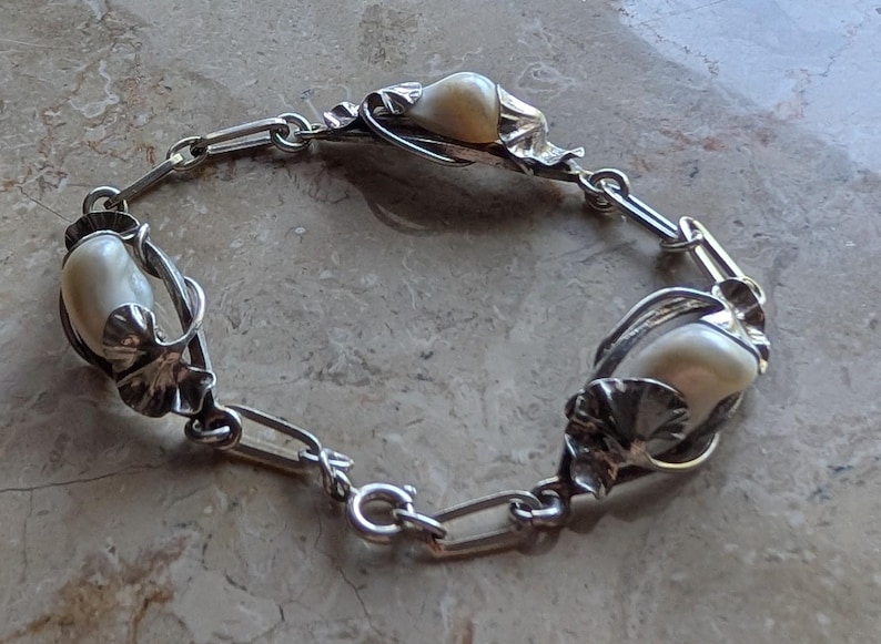 May include: Silver-toned bracelet featuring three large, off-white, oval-shaped beads. The beads are set in ornate, leaf-like settings and connected by a chain link design. The bracelet is displayed on a light-colored surface.