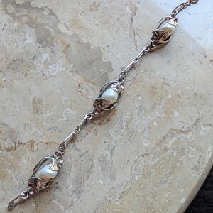 May include: A silver bracelet featuring three large, lustrous pearls encased in decorative settings. The bracelet has a delicate chain design with intricate floral accents, creating an elegant and timeless piece of jewelry.