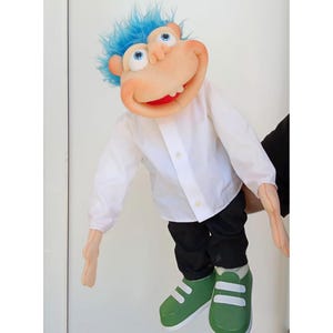May include: A hand puppet featuring a character with bright blue hair, large eyes, and a wide mouth. The puppet wears a long-sleeved white button-down shirt, black trousers, and green sneakers with white straps. The skin tone is light peach.