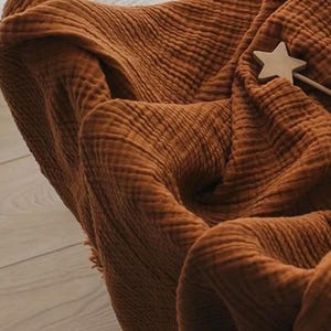 May include: A brown waffle weave throw blanket with frayed edges. The blanket is folded and draped over a chair.