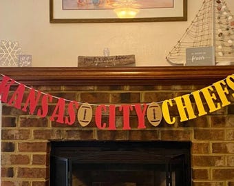 May include: A red, yellow, and brown banner with the words "Kansas City Chiefs" and two footballs.