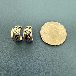 Puede incluir: Un par de pendientes de aro dorados con un patrón geométrico de diamantes repetitivo, mostrados junto a una moneda de 25 centavos de dólar estadounidense como escala para demostrar el tamaño de las piezas de joyería.