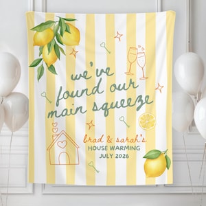 Könnte beinhalten: Ein gelb-weiß gestreifter Einweihungsbanner mit dem Text "we've found our main squeeze". Das Banner zeigt Illustrationen von Zitronen, Schlüsseln, Sektgläsern und einem Haus. Auf dem Banner steht "brad & sarah's HOUSE WARMING JULY 2026".