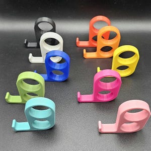 以下が含まれることがあります： 黒、白、青、オレンジ、黄色、緑、ピンク、水色など、さまざまな色のカラフルな3Dプリントの携帯電話スタンドのコレクション。 各スタンドは、リンググリップと電話を保持するための小さな棚を備えています。