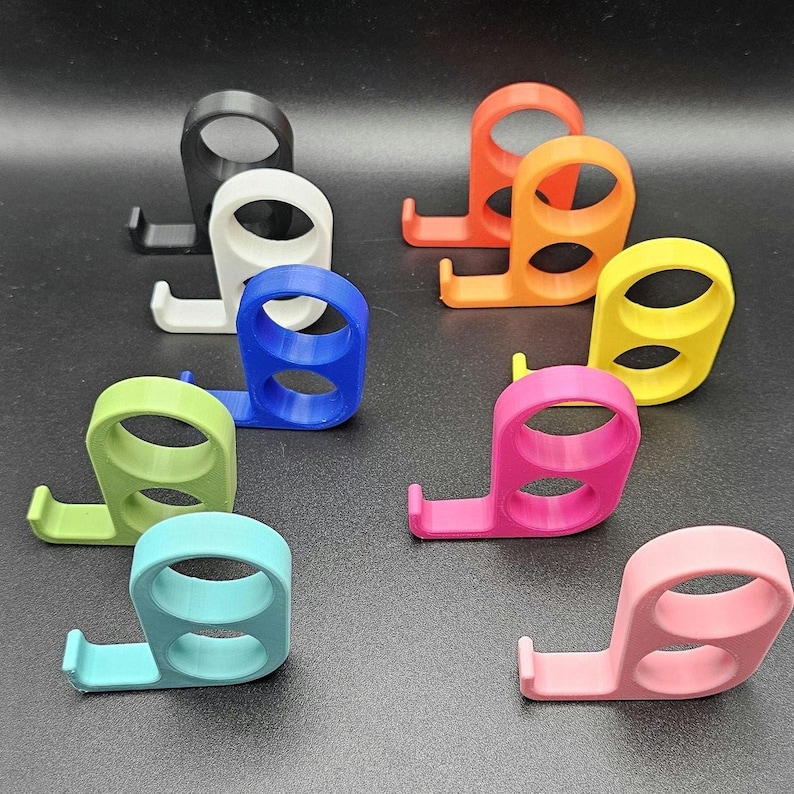 以下が含まれることがあります： 黒、白、青、オレンジ、黄色、緑、ピンク、水色など、さまざまな色のカラフルな3Dプリントの携帯電話スタンドのコレクション。 各スタンドは、リンググリップと電話を保持するための小さな棚を備えています。