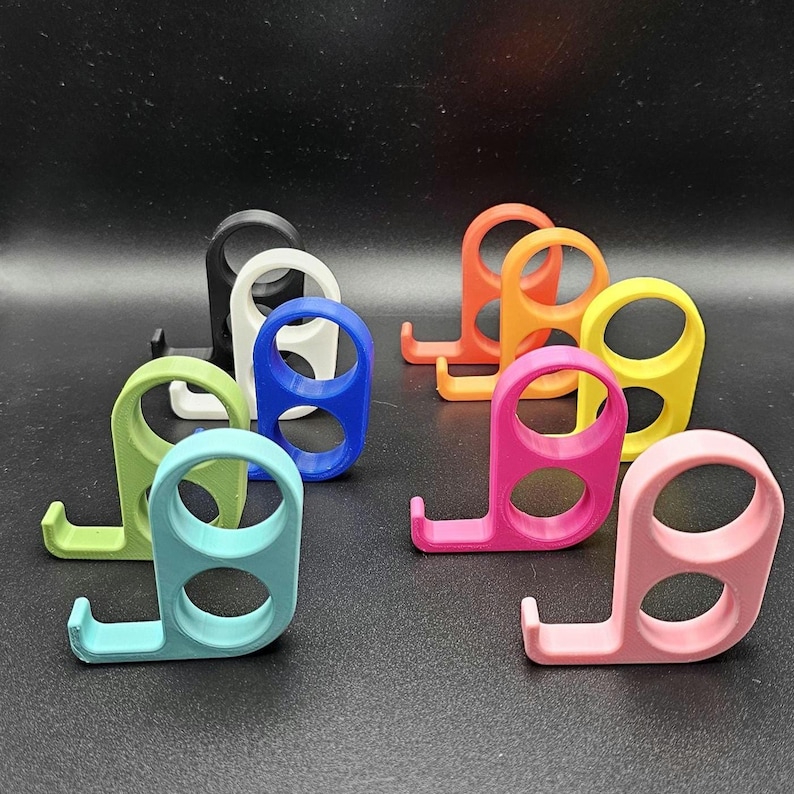 以下が含まれることがあります： ピンク、オレンジ、黄色、緑、青、白、黒など、さまざまな色のカラフルな3Dプリントの電話スタンドのコレクション。各スタンドは、湾曲したベースと、2つの穴のある円形のトップを備えており、電話を保持するように設計されています。