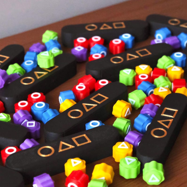 May include: A collection of colorful game pieces and black rectangular game boards. The game pieces are in various colors, including red, blue, green, yellow, and purple. The game boards have gold symbols and text.