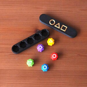 May include: A black wooden game piece holder with five slots, a black rectangular piece with gold shapes, and six colorful game pieces with geometric shapes. The pieces are yellow, purple, red, green, and blue.