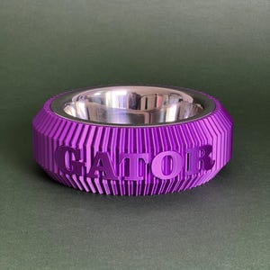 Puede incluir: Tazón para mascotas de color morado con interior plateado y la palabra "GATOR" en relieve en el lateral.