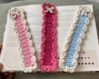 May include: Three crocheted bookmarks with scalloped edges. One is pink with white trim, one is blue with white trim, and one is pink with white trim. The bookmarks are laying on a book with the text "Finding Focus" and "Rest Zones" visible.