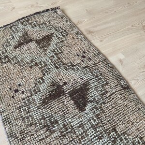 May include: A vintage rug with a geometric pattern in shades of brown, beige, and white. The rug has a distressed look and is made of a woven material.