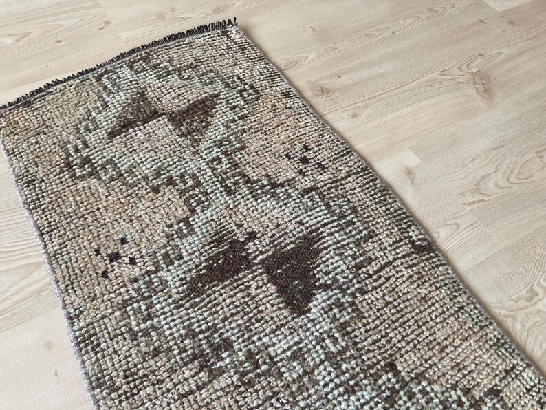 May include: A vintage rug with a geometric pattern in shades of brown, beige, and white. The rug has a distressed look and is made of a woven material.
