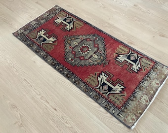 May include: A rectangular, red and gray patterned rug with a central medallion design and repeating bird-like motifs. The rug has a distressed, vintage appearance and is likely made of woven material.